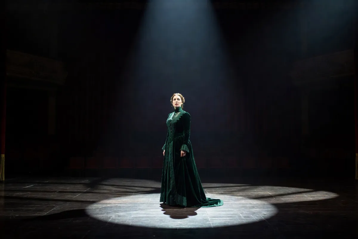 Comédienne en robe d'époque seule sur une scène sombre sous un projecteur