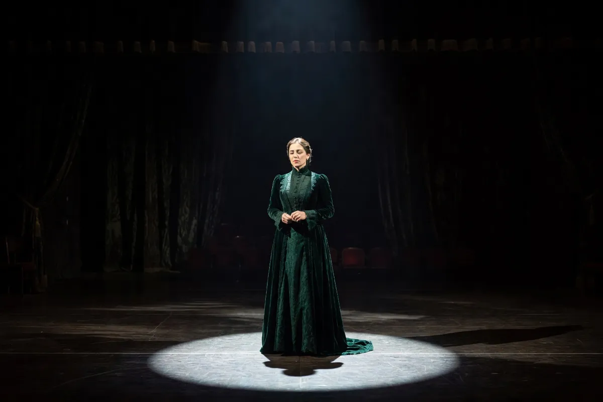 Comédienne en robe d'époque seule sur une scène sombre sous un projecteur