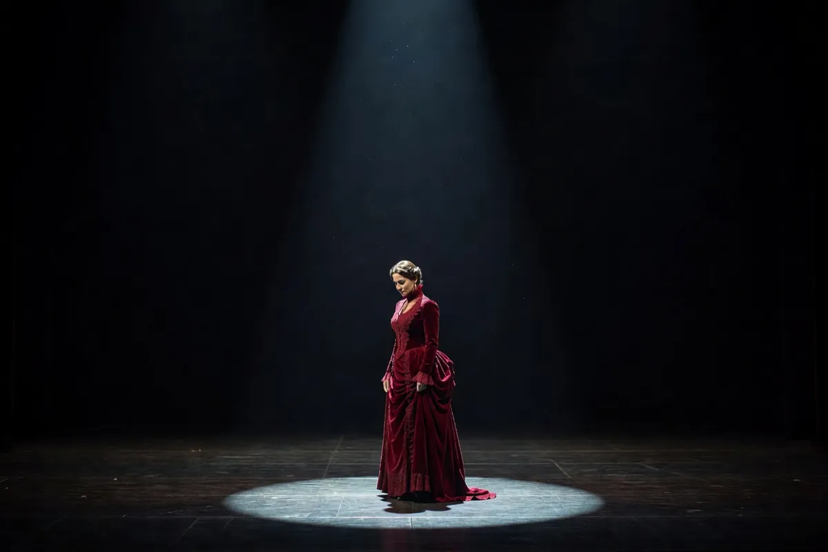 Comédienne en robe d'époque seule sur une scène sombre sous un projecteur