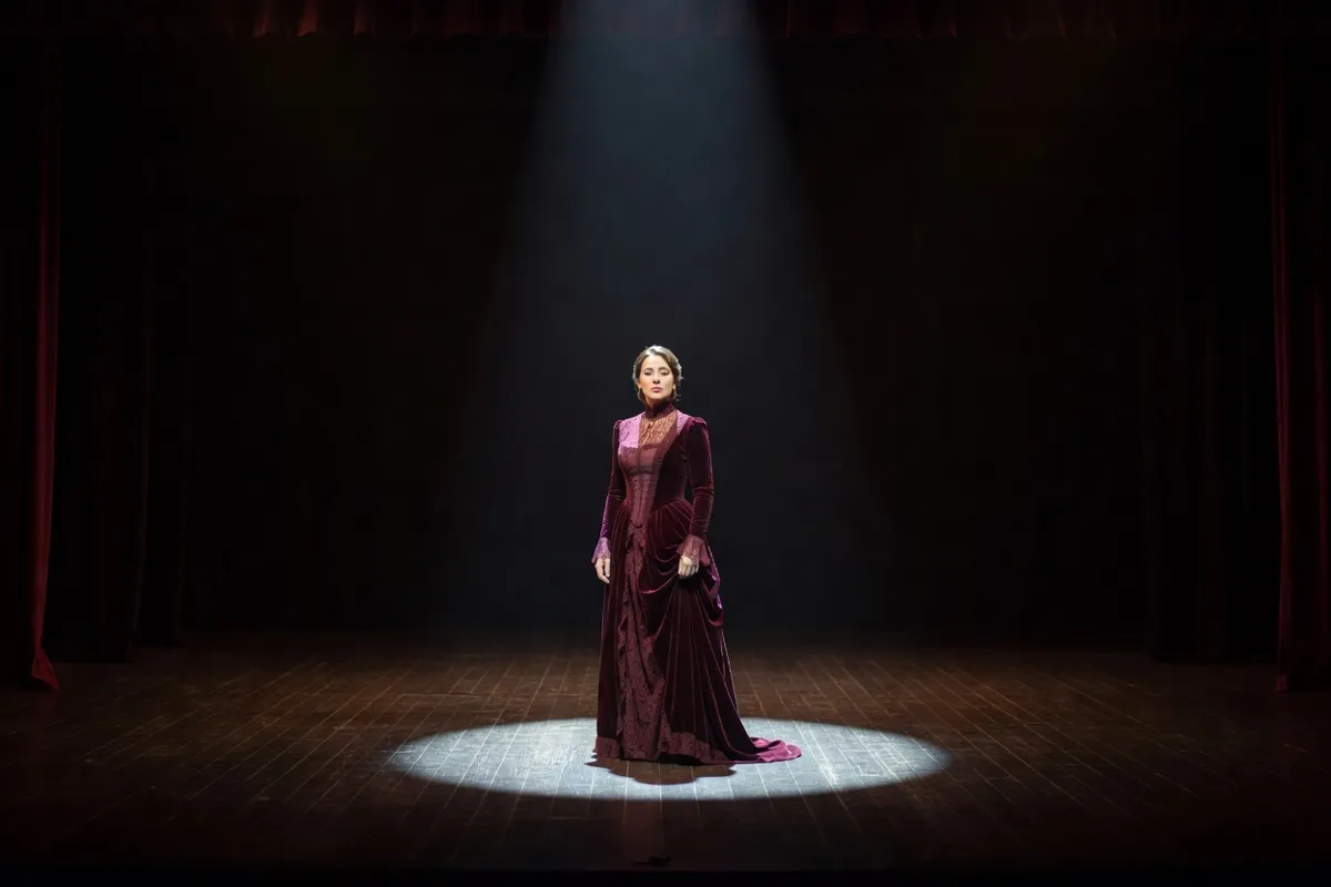 Comédienne en robe d'époque seule sur une scène sombre sous un projecteur