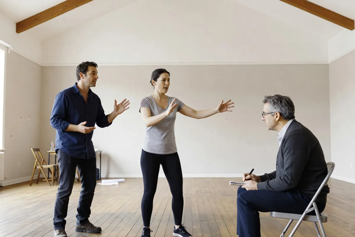 Comédiens en répétition dans une salle claire avec un metteur en scène prenant des notes
