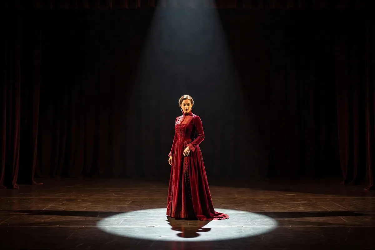 Comédienne en robe d'époque seule sur une scène sombre sous un projecteur