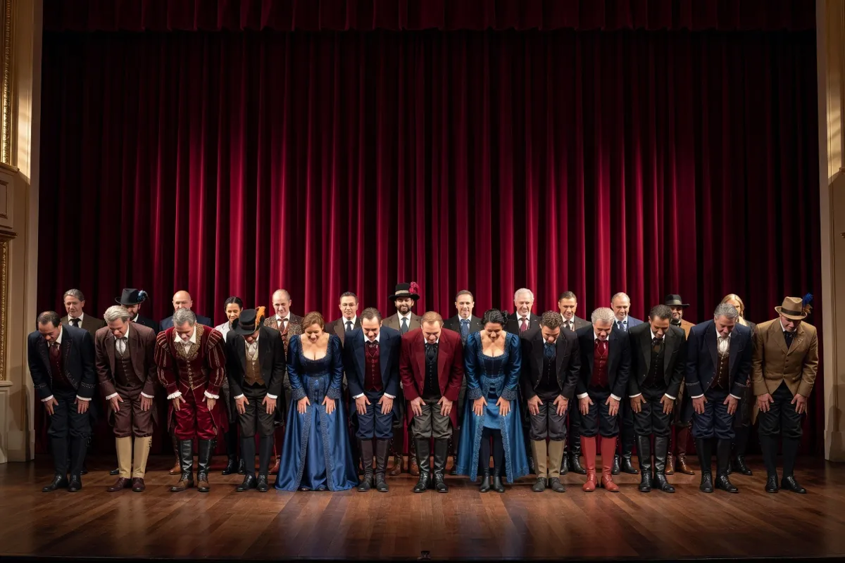 Comédiens en costumes saluant devant un rideau rouge sur une scène de théâtre