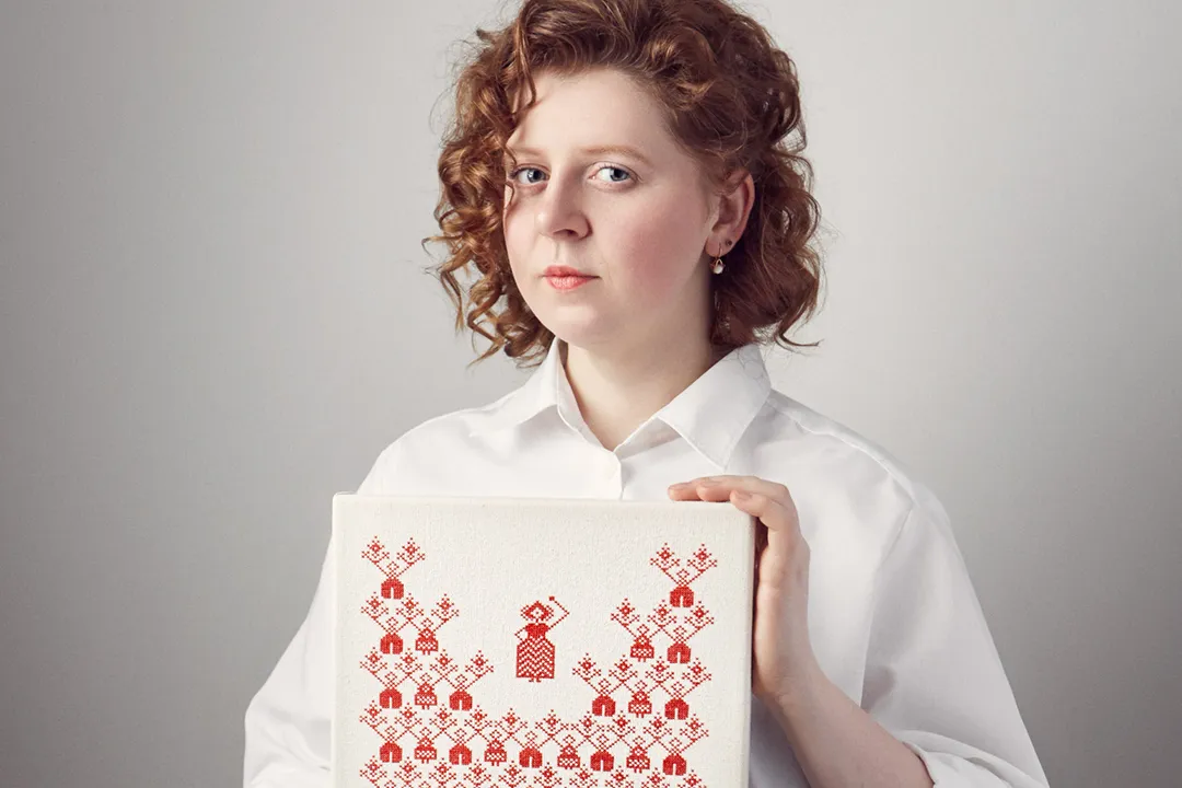 Rufina Bazlova présentant une broderie de la série "The History of Belarusian Vyzhyvanka", motifs rouge et blanc, mémoire de la répression