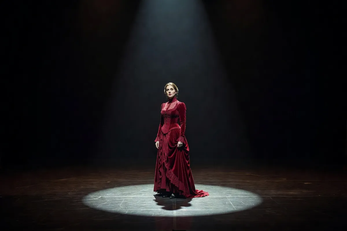 Comédienne en robe d'époque seule sur une scène sombre sous un projecteur
