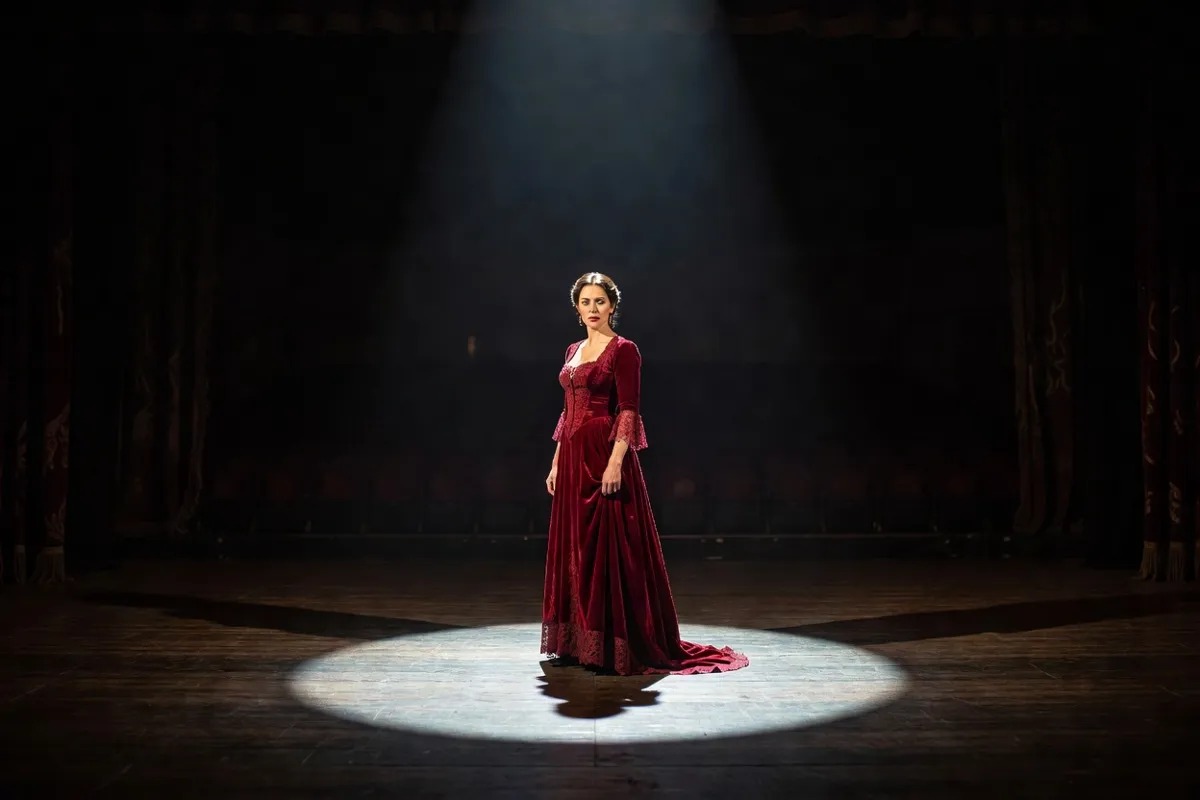 Comédienne en robe d'époque seule sur une scène sombre sous un projecteur