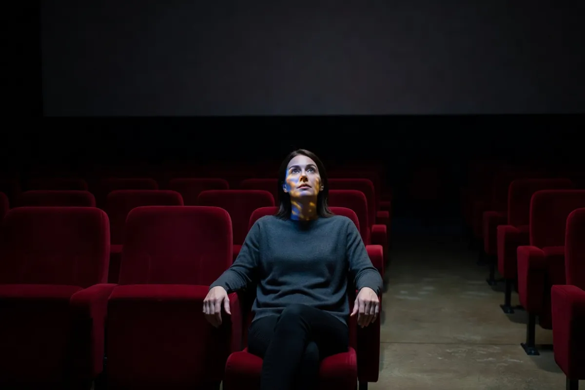 Spectatrice dans une salle de cinéma obscure, visage éclairé par l'écran
