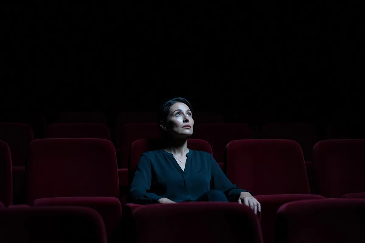 Spectatrice dans une salle de cinéma obscure, visage éclairé par l'écran