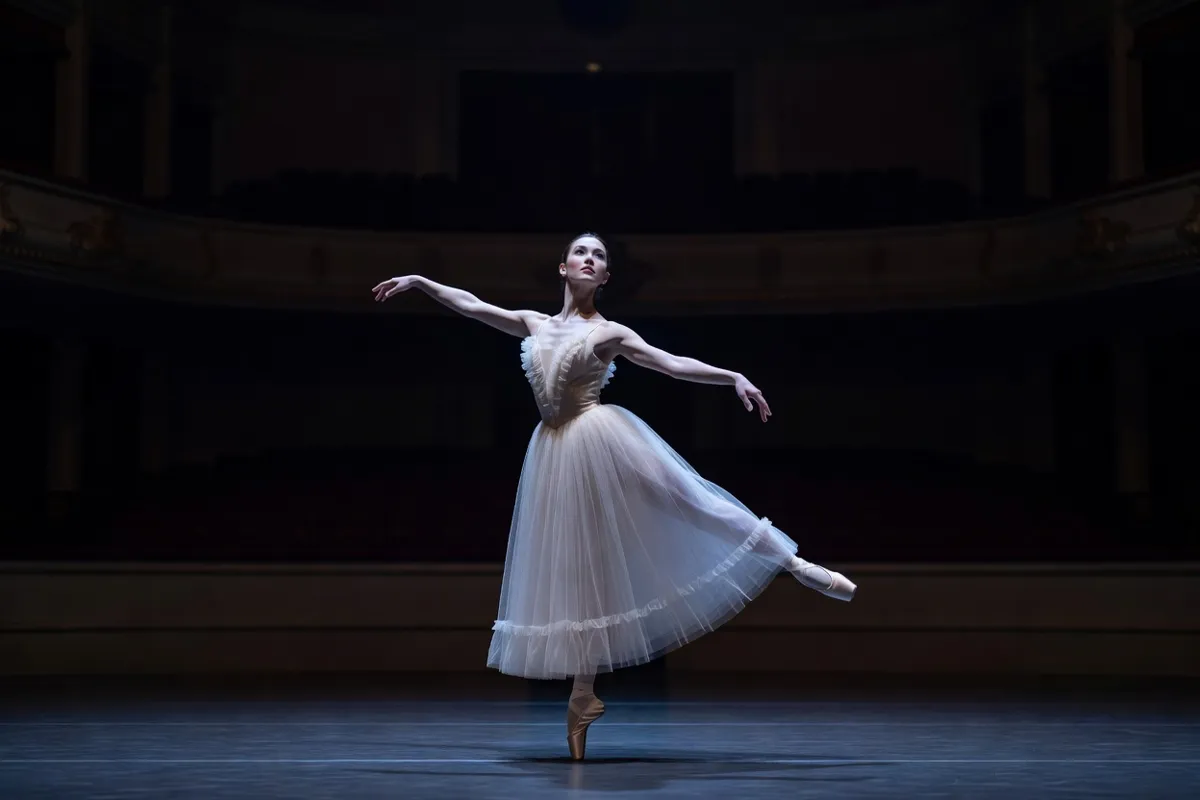 Danseuse en tutu romantique sur une scène de théâtre sous une lumière bleutée