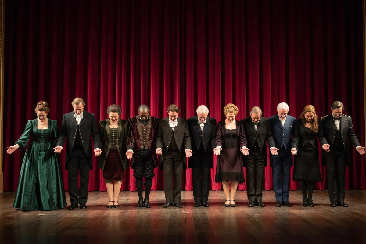 Comédiens en costumes saluant devant un rideau rouge sur une scène de théâtre