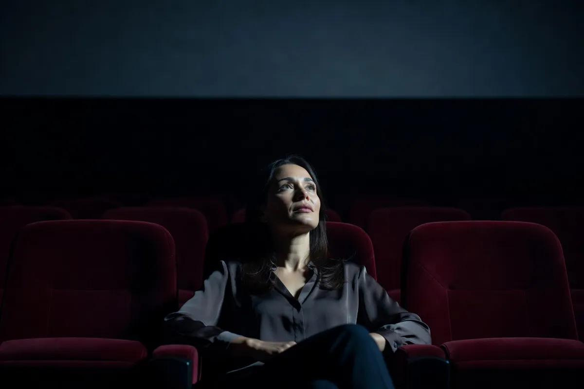 Spectatrice dans une salle de cinéma obscure, visage éclairé par l'écran