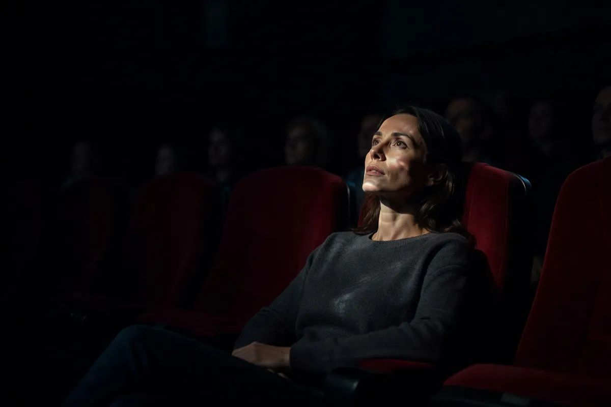 Spectatrice dans une salle de cinéma obscure, visage éclairé par l'écran