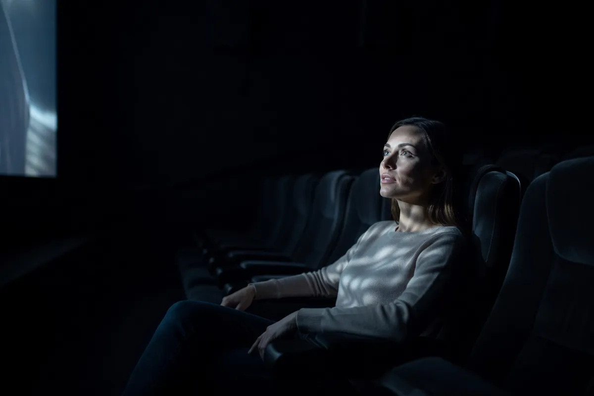 Spectatrice dans une salle de cinéma obscure, visage éclairé par l'écran